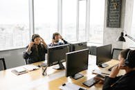 Focused call center agents working at computers with headsets in a bright office setting.